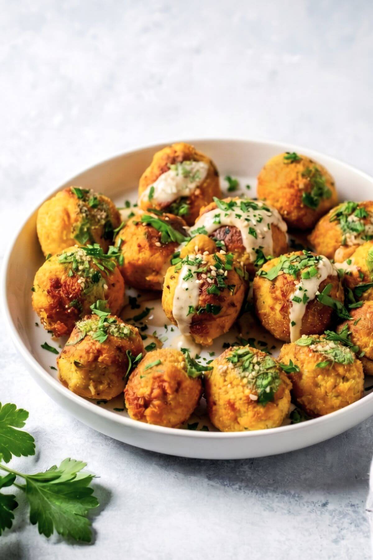Bowl full of vegan chickpea meatballs garnished with fresh chopped parsley and tahini