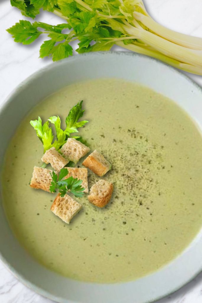 A bowl of Cream of Celery Soup garnished with celery leaves and croutons