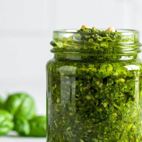 Jar of vegan basil pesto with basil leaves in the background