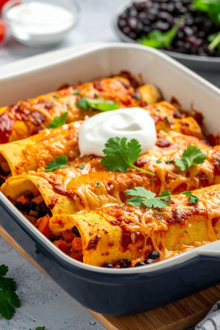 Baking pan of Vegan Sweet Potato and Black Bean Enchilada garnished with vegan sour cream