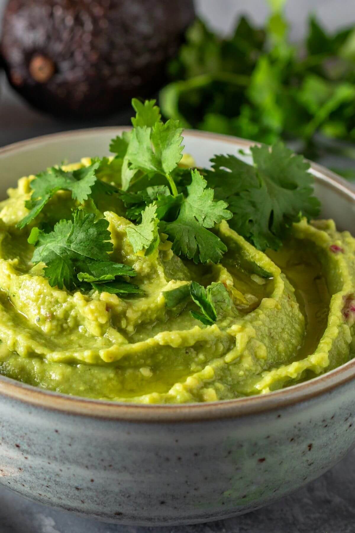Bowl of guacamole garnished with cilantro and an avocado next to it