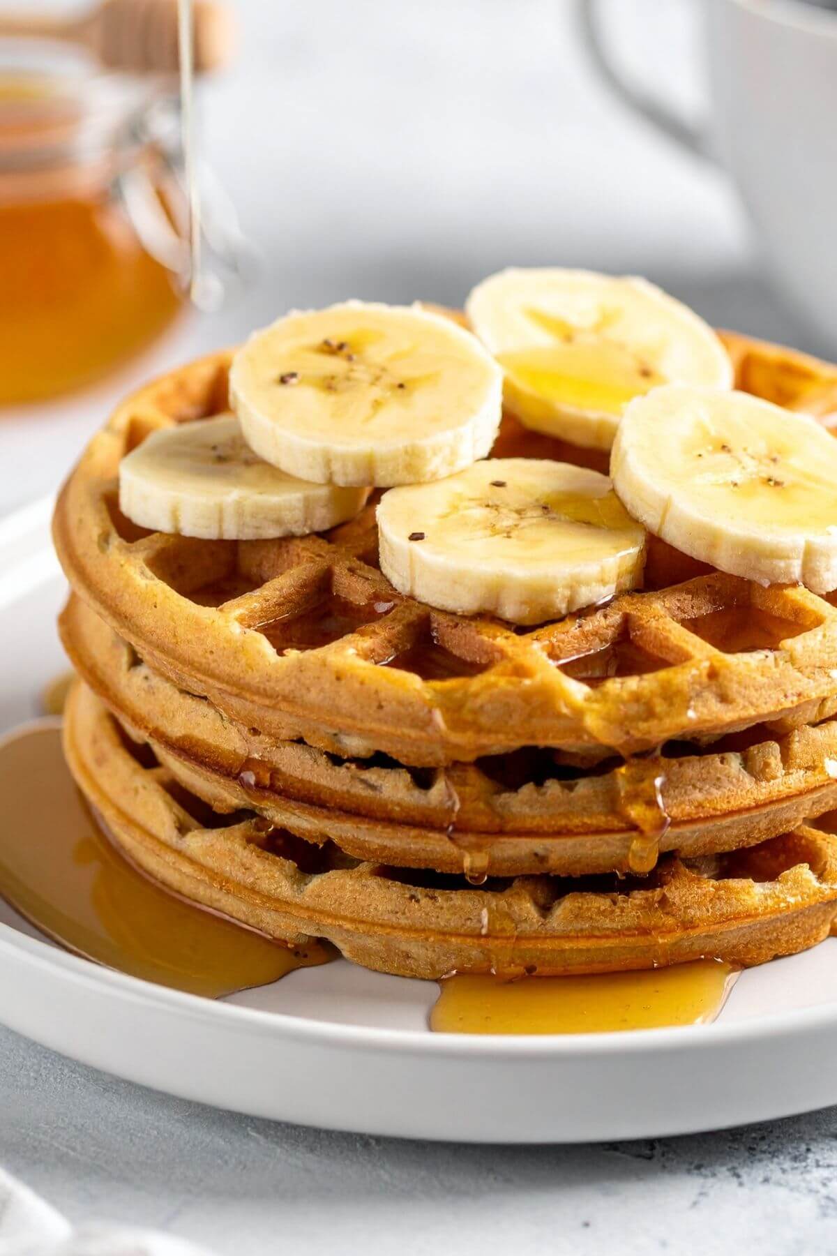 Stack of Easy Vegan Waffles with sliced bananas and maple syrup over them