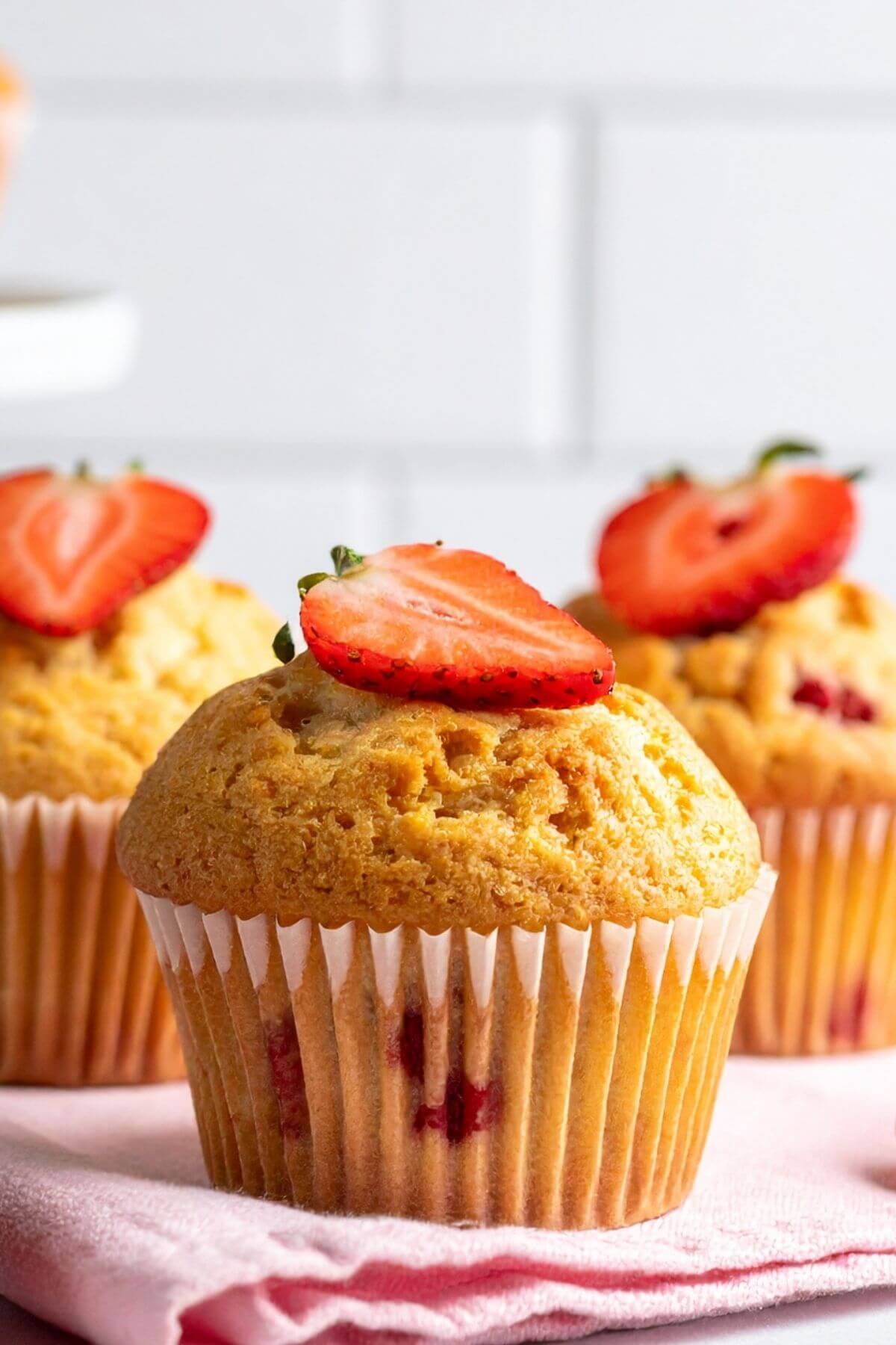 Vegan Strawberry Muffins with a sliced strawberry on top, on a pink napkin