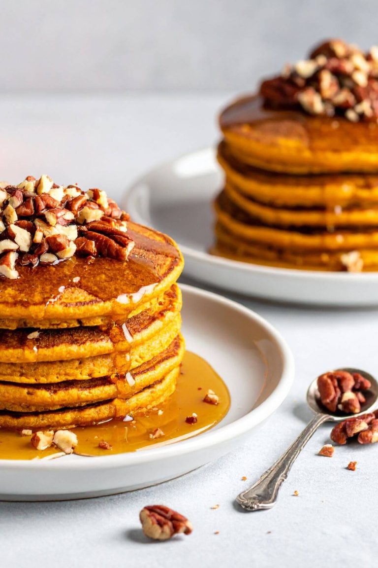 Two plates of Vegan pumpkin pancakes toped with chopped nuts and maple syrup