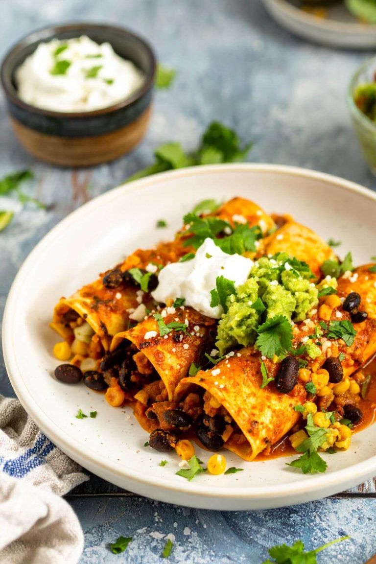 3 Cauliflower Black Bean Enchiladas on a plate garnished with guacamole and vegan sour cream