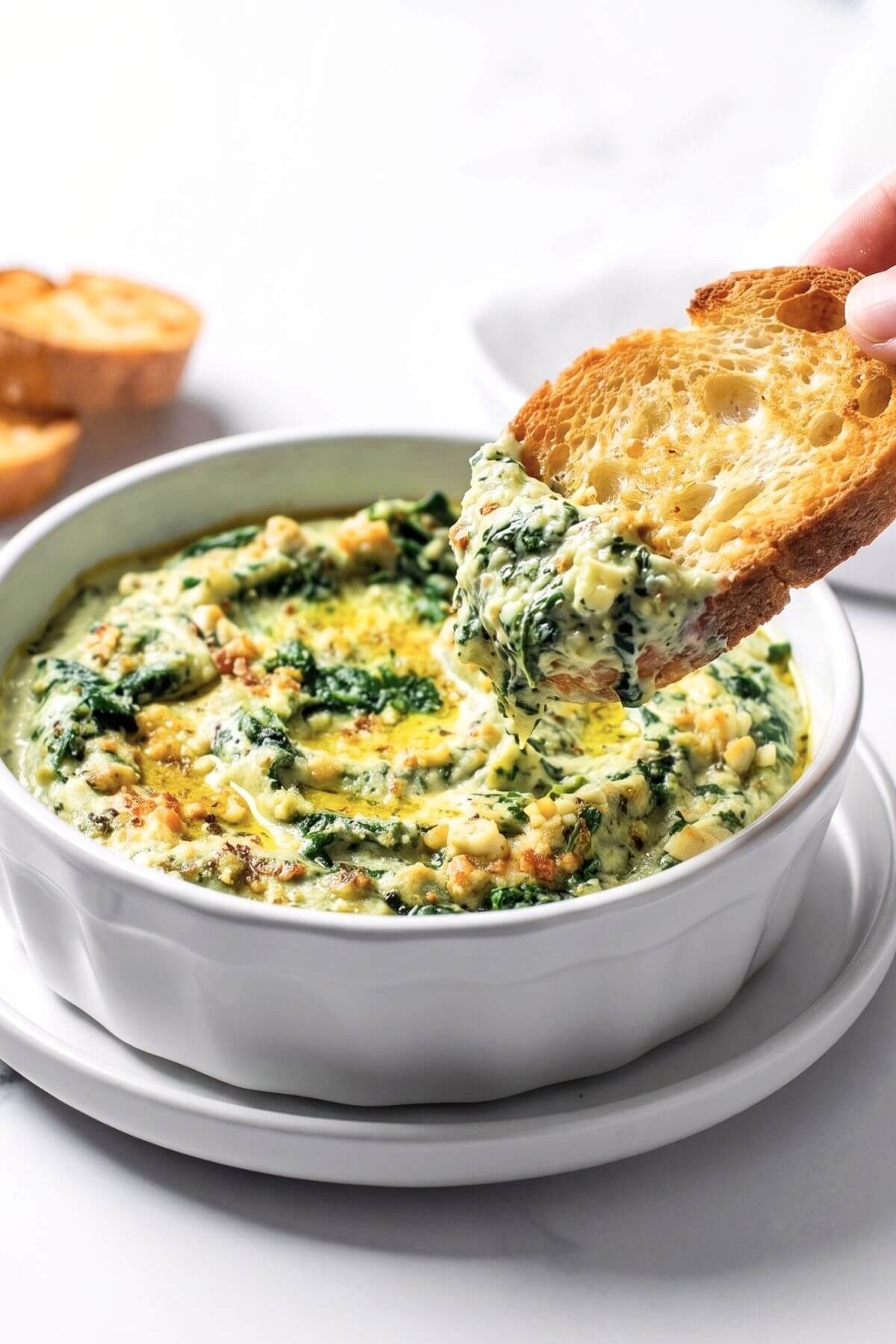 Vegan Spinach Artichoke Dip with bread slices and one dipped into dip