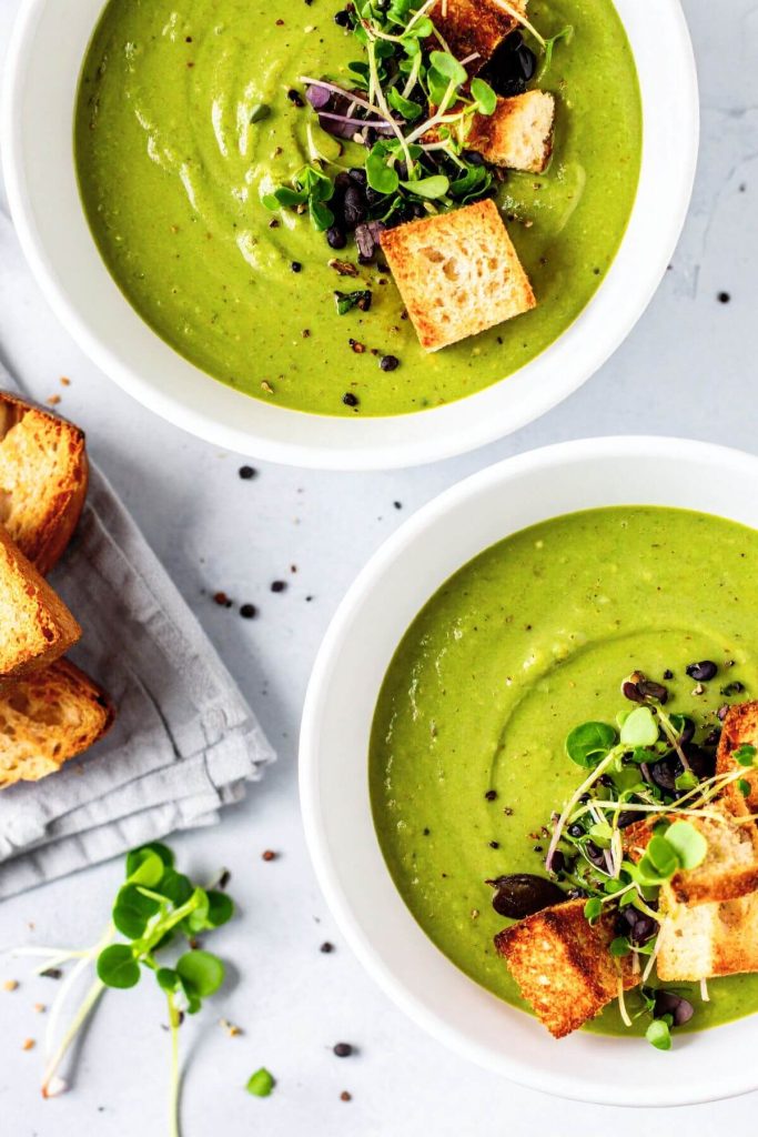 Two bowls of Vegan Broccoli Pea Soup garnished with microgreens and croutons