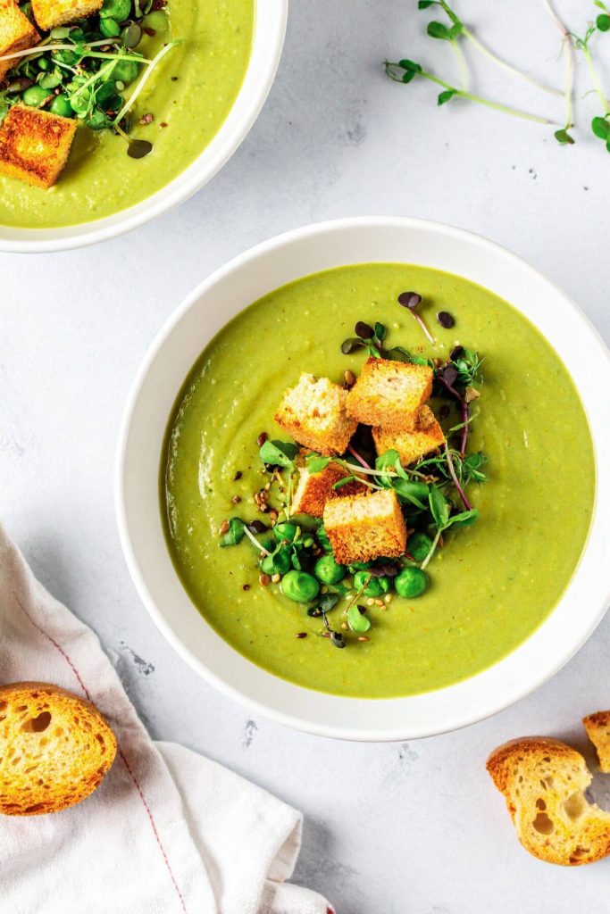Two bowls of Vegan Broccoli Pea Soup garnished with microgreens and croutons