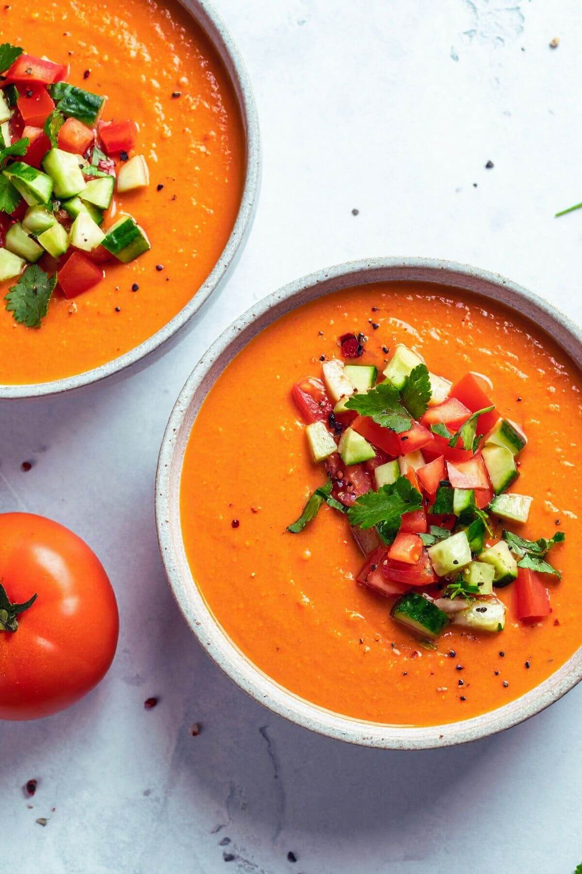Two Bowls of vegan Gazpacho Soup with garnish of diced tomatoes, cucumber, onions, and herbs for lunch or dinner
