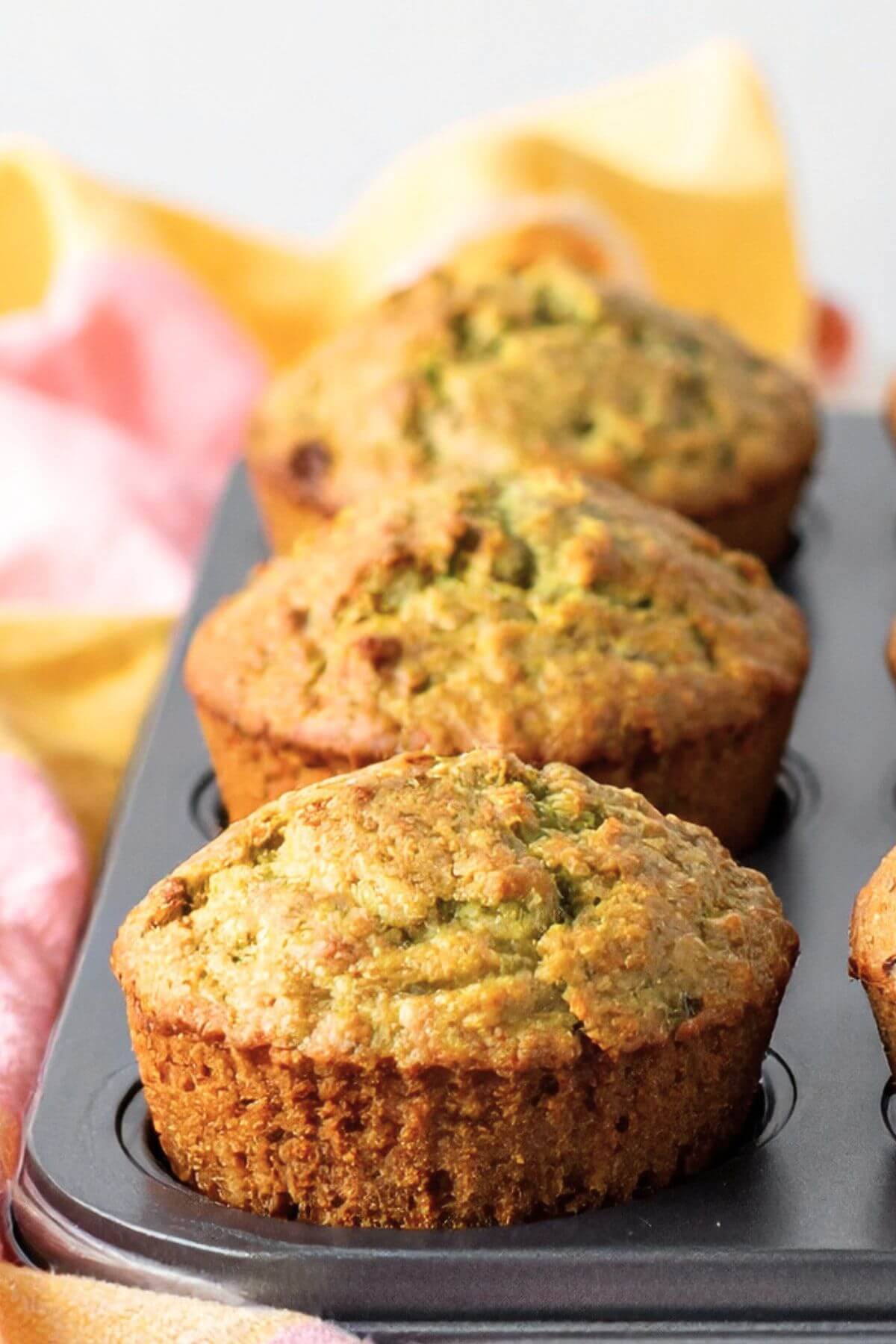 Close-up of vegan zucchini muffins baked in a muffin tin with soft golden tops and fresh zucchini flecks