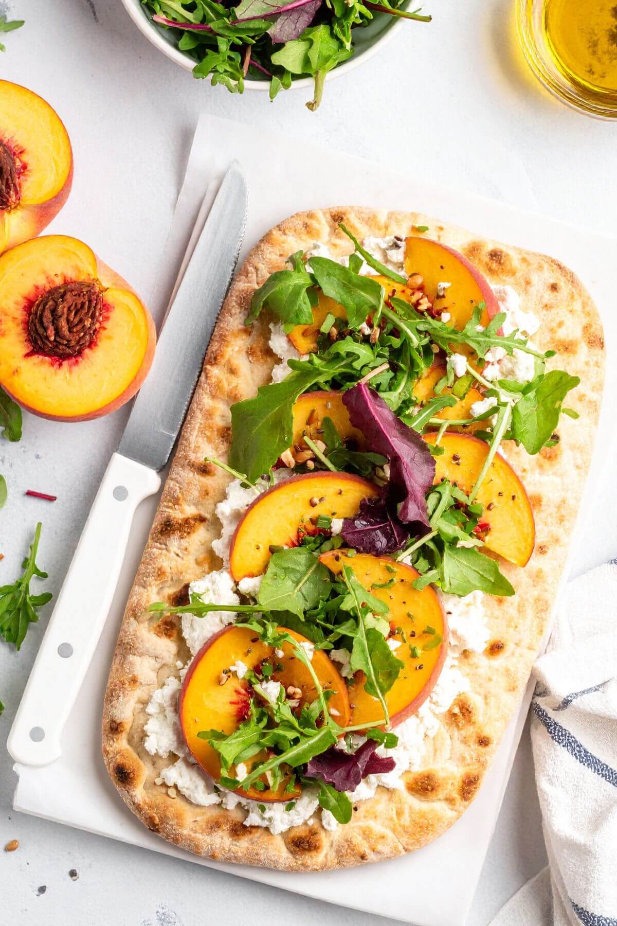 A flatbread with vegan ricotta, sliced peaches and mixed greens