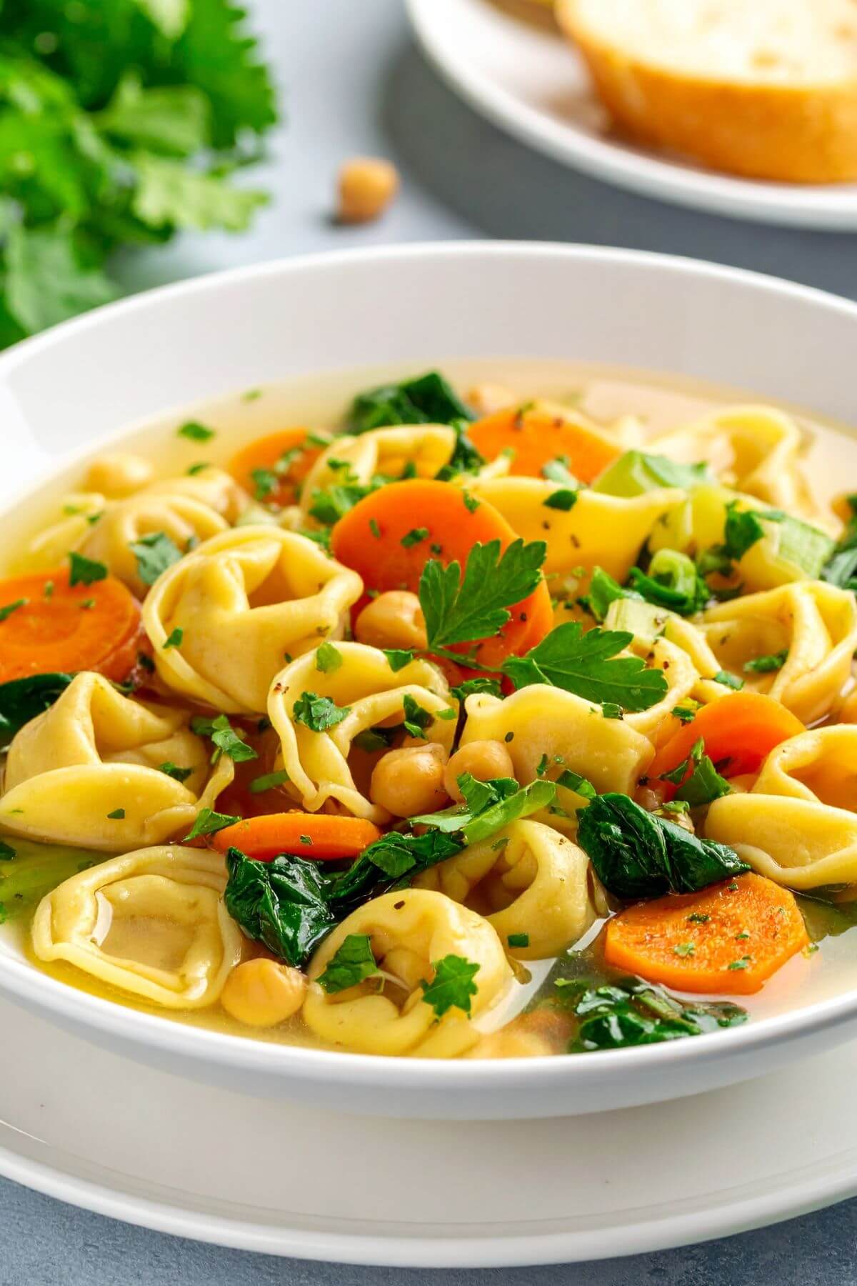 A bowl of Lemon Tortellini Soup with sliced carrots, celery and s;inach with added chickpeas