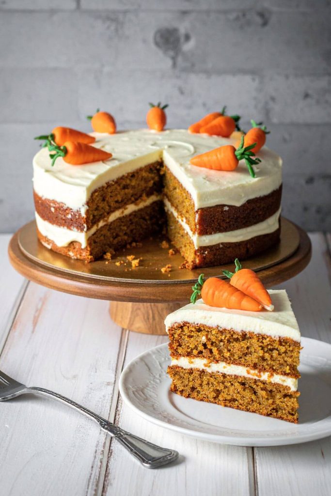 Vegan Carrot Cake decorated with vegan cheese frosting and carrot decors.