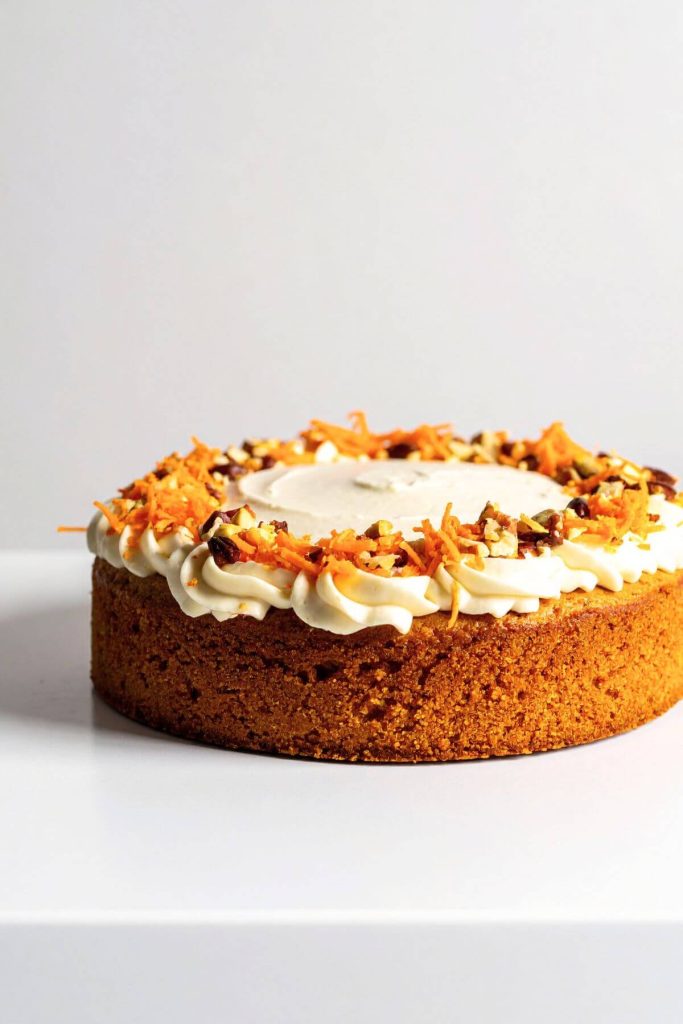 single layer vegan carrot cake with cream cheese frosting with chopped nuts and grated carrot garnish