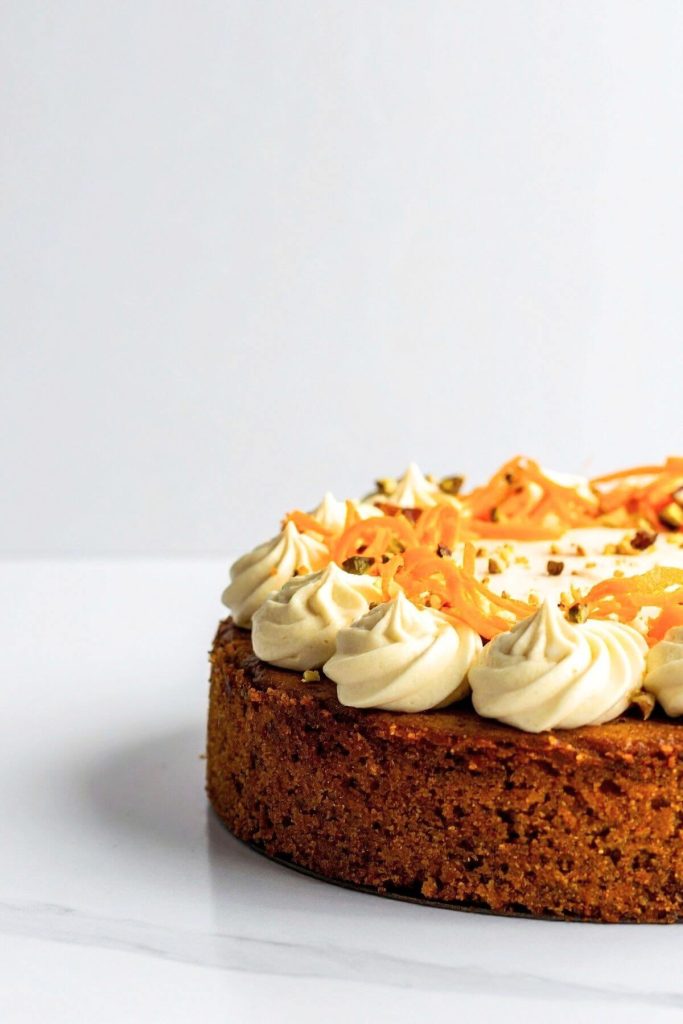 single layer vegan carrot cake with cream cheese frosting with chopped nuts and grated carrot garnish