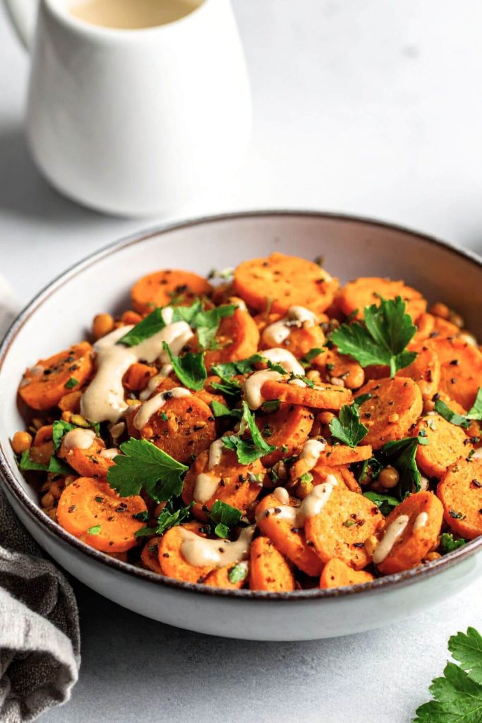 Roasted carrot and lentil salad with creamy tahini dressing being drizzled over top