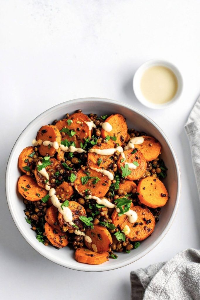 Roasted carrot and lentil salad with creamy tahini dressing being drizzled over top