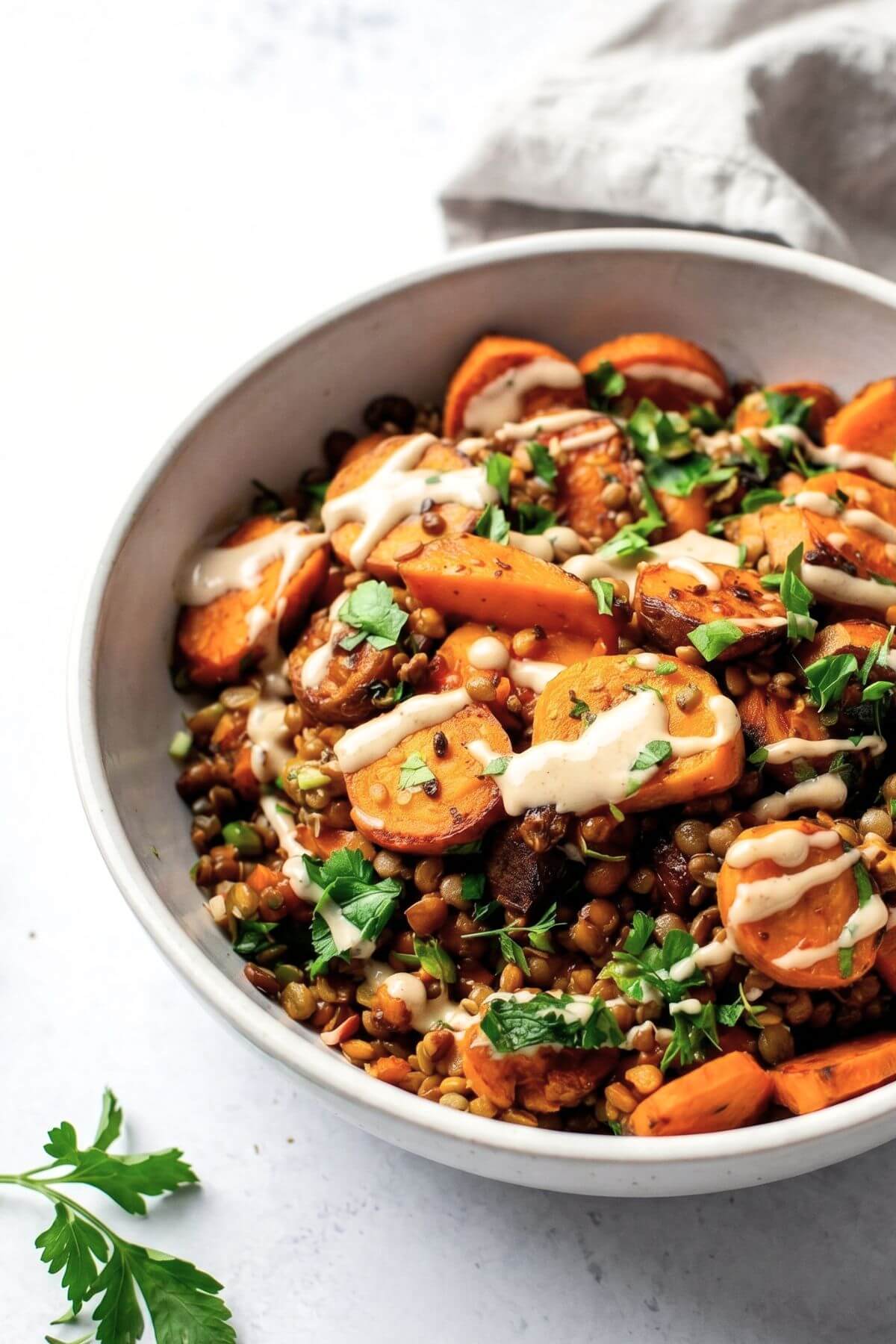 Roasted carrot and lentil salad with creamy tahini dressing being drizzled over top