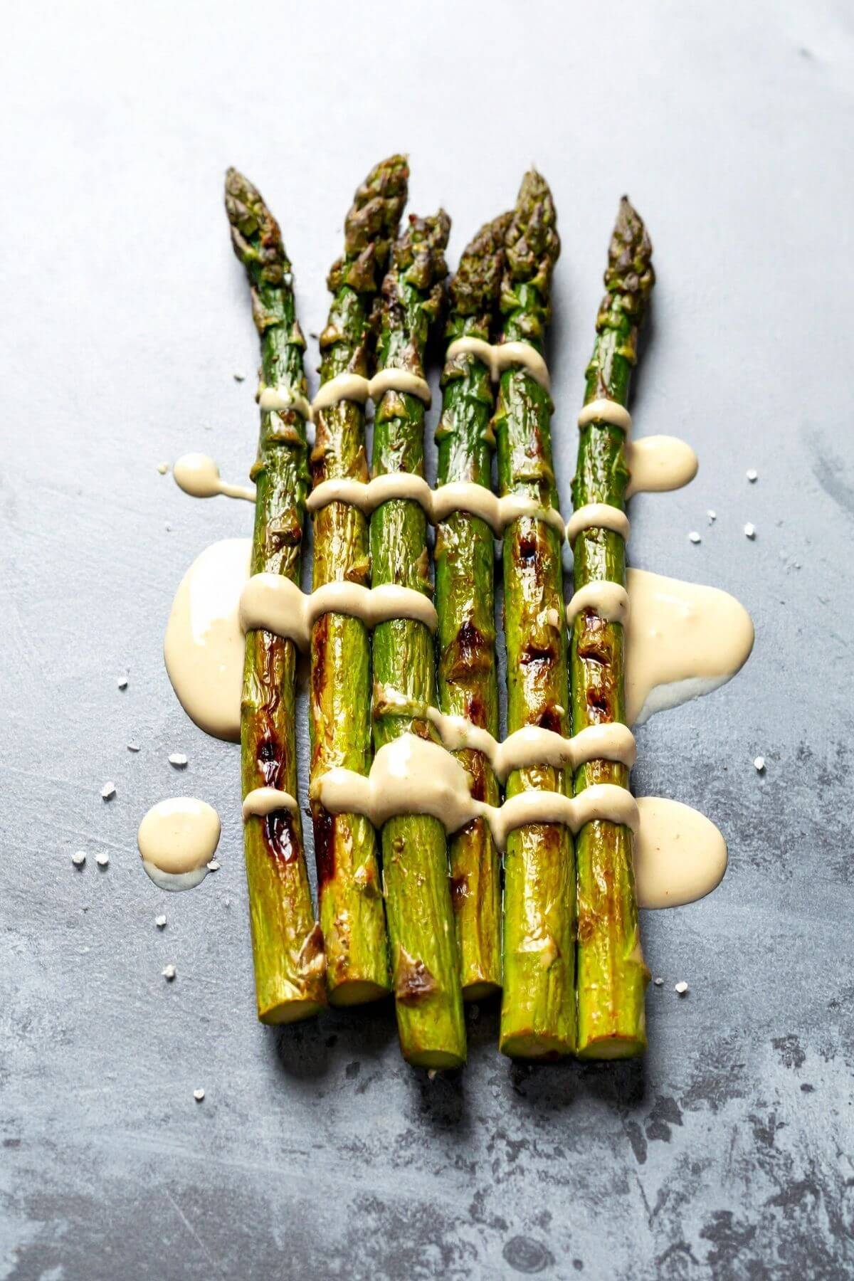 Pretty Roasted Asparagus on marble with Creamy Lemon Tahini Sauce drizzled onver it
