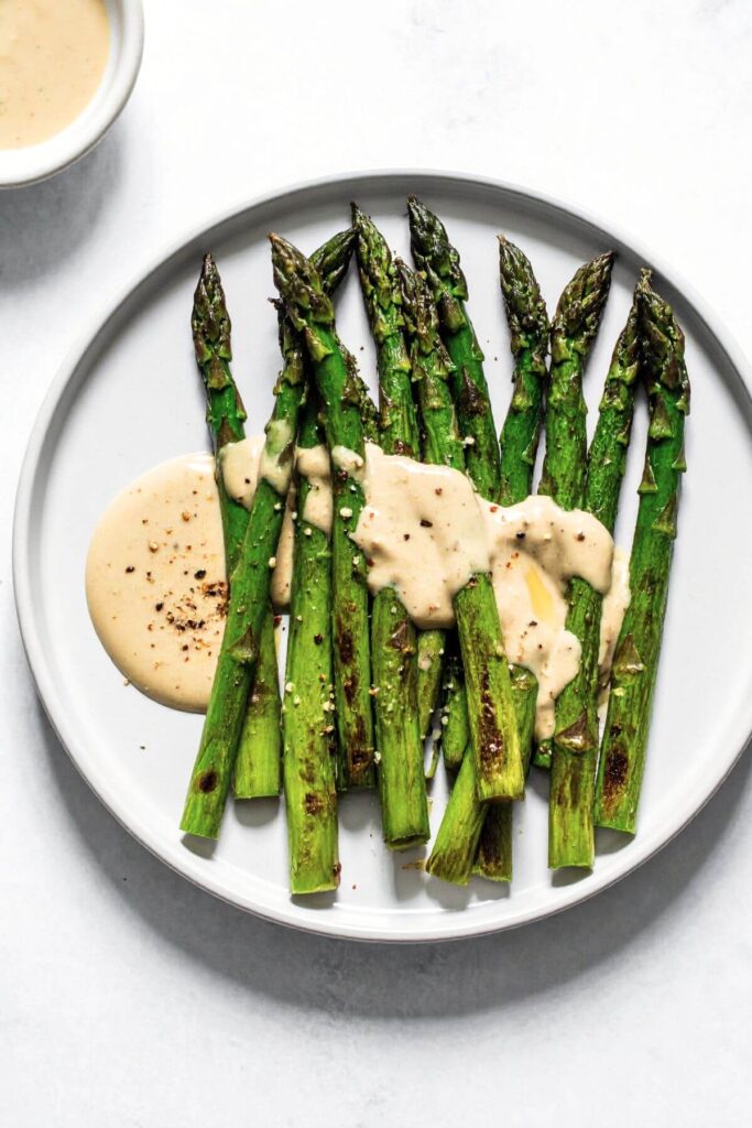 Roasted asparagus with tahini drizzle and garlic on a white plate