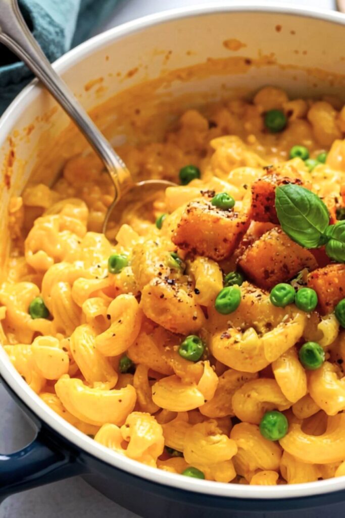 Pot of no-nut, vegan, gluten-free butternut squash macaroni and cheese with peas. Garnished with squash cubes and peas