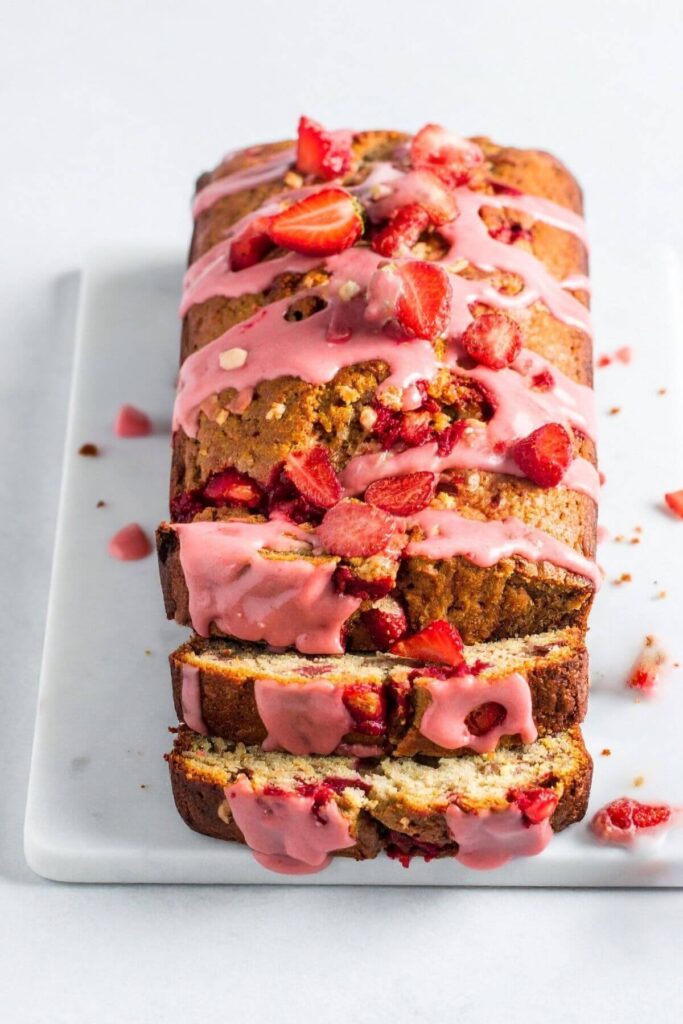 Strawberry banana bread topped with pink glaze and fresh strawberries on a serving platter.