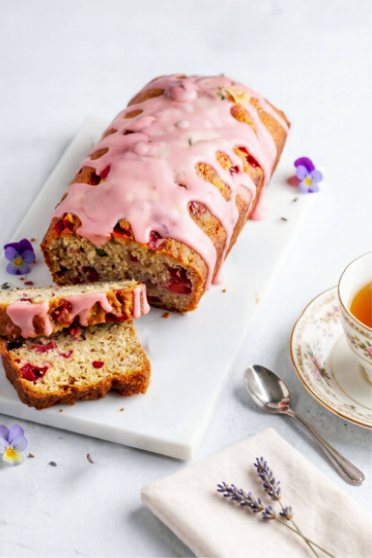 Vegan banana strawberry bread with pink strawberry glaze sliced on a white marble board with cup of tea