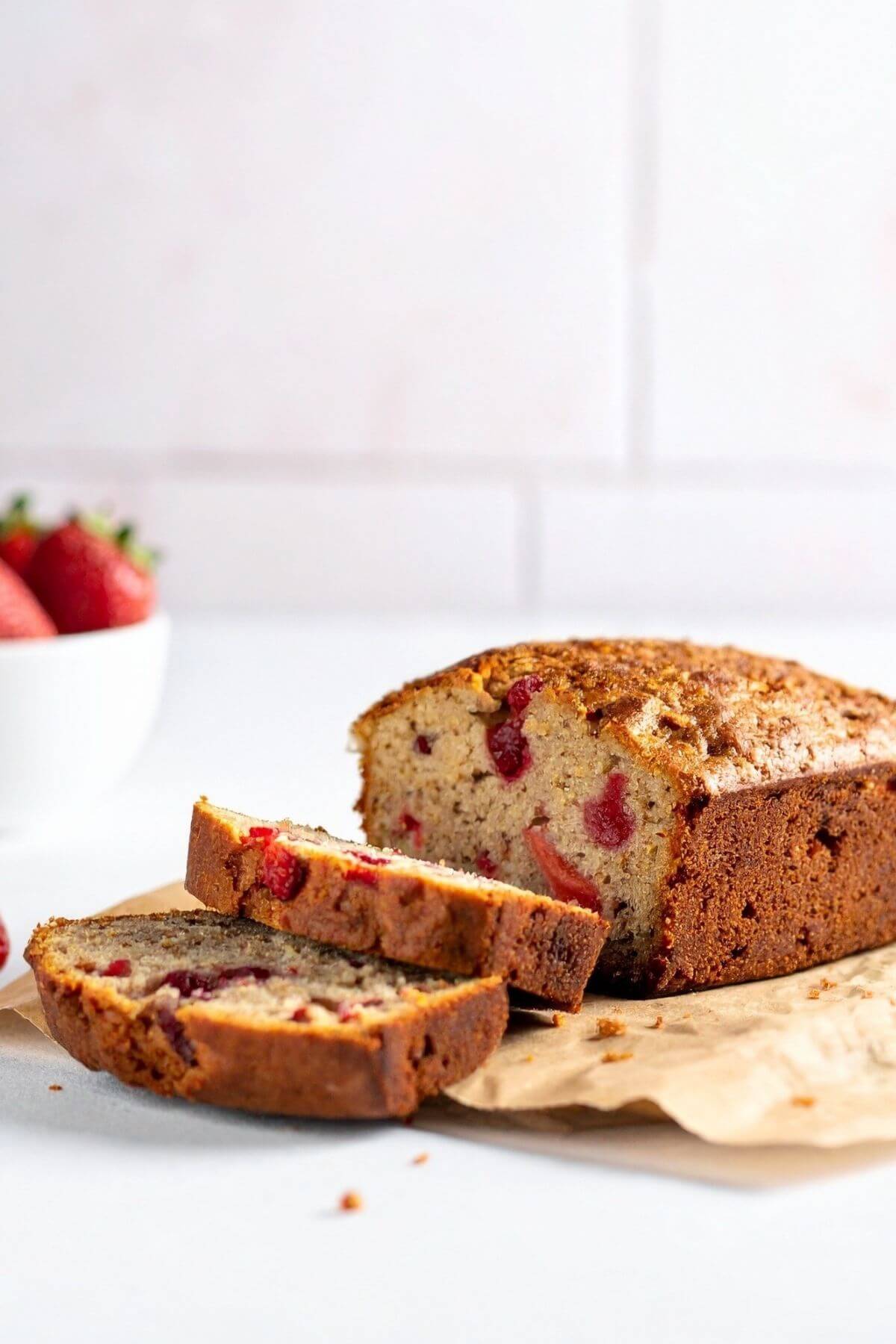 Homemade strawberry banana bread on a wooden board with fresh strawberries